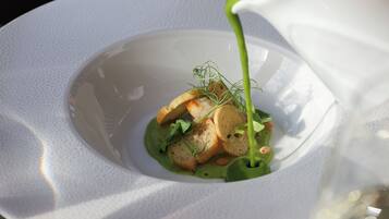 A white plate with a green sauce being poured over a dish with bread and greens.