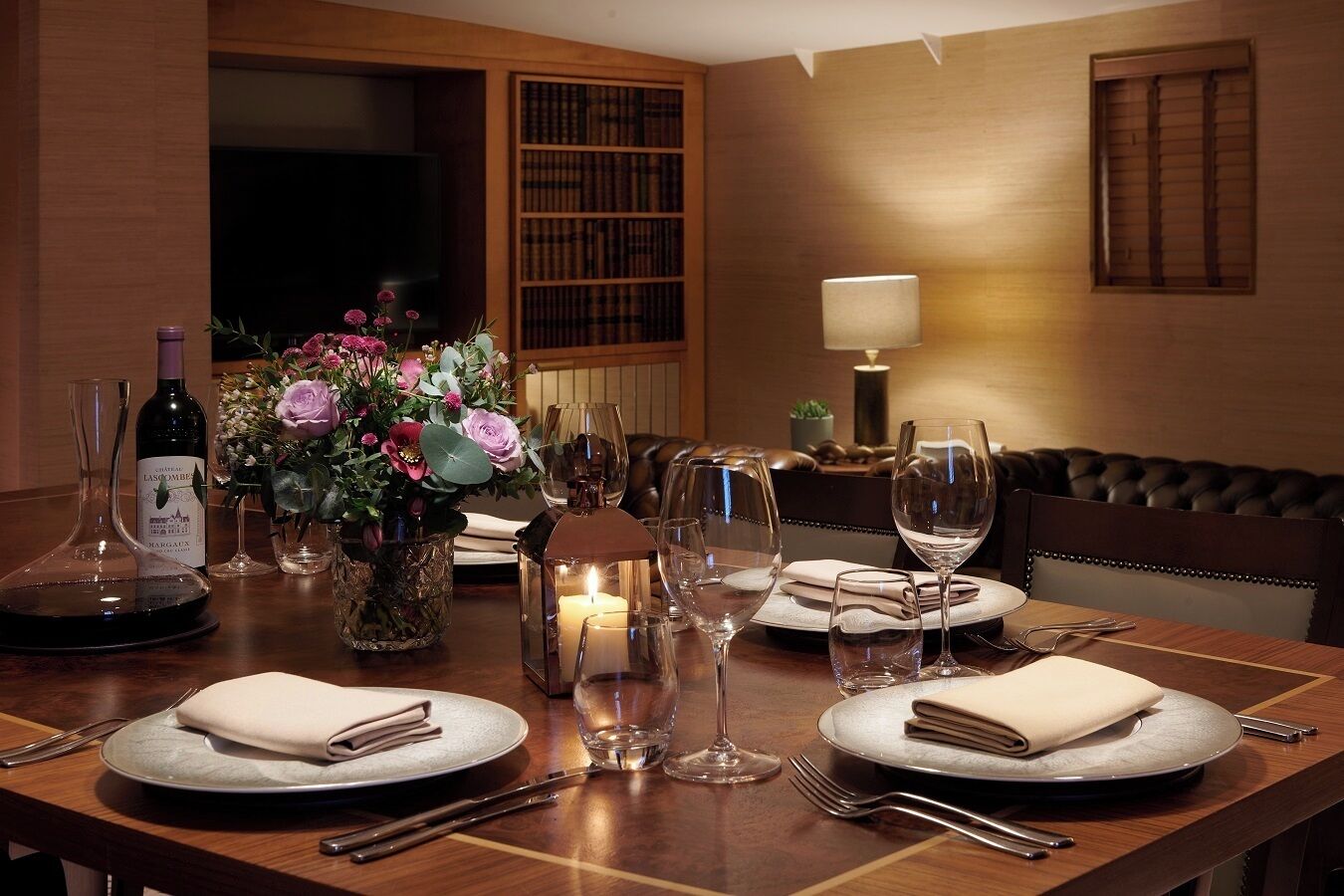 Une table à manger dressée pour quatre personnes, avec des verres à vin, une bougie et un centre de table composé de fleurs.