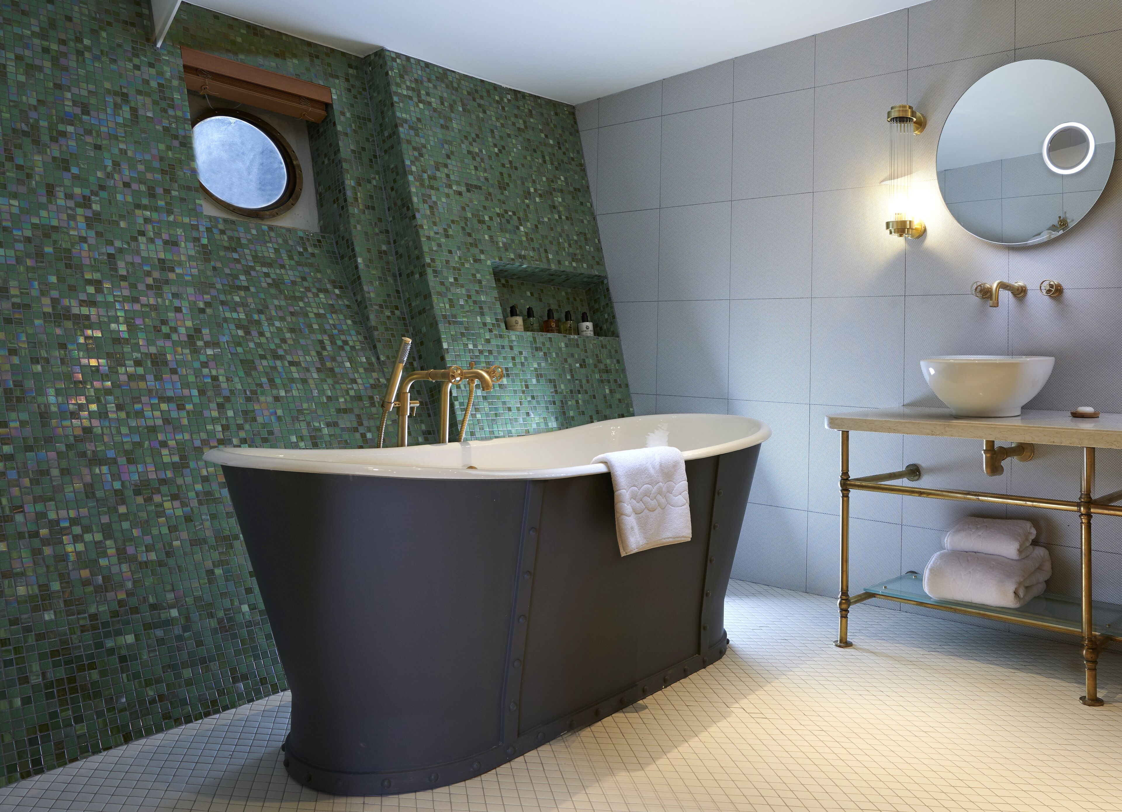 A modern bathroom with a freestanding bathtub, a round mirror with a light, and a sink with a bowl.