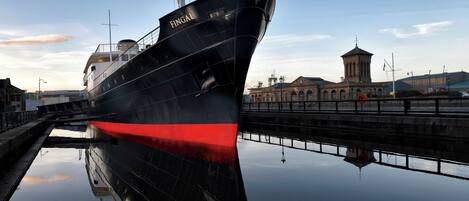 A large ship docked at a port with a clear sky and a building in the background.