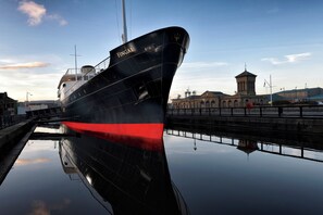 A large ship docked at a port with a clear sky and a building in the background. - Fingal - A Luxury Floating Hotel (Edinburgh)