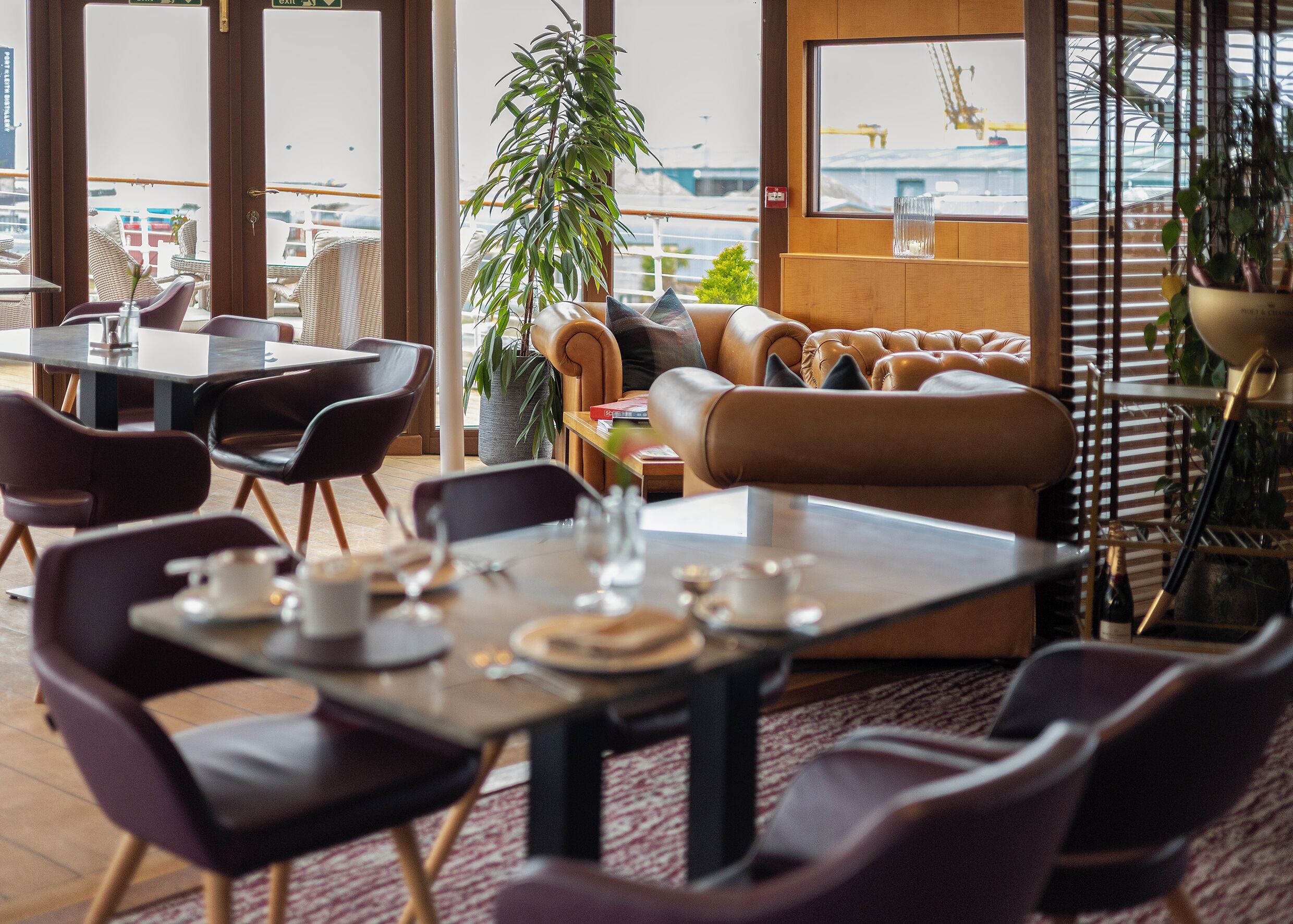 A restaurant with tables, chairs, a sofa, and a potted plant.