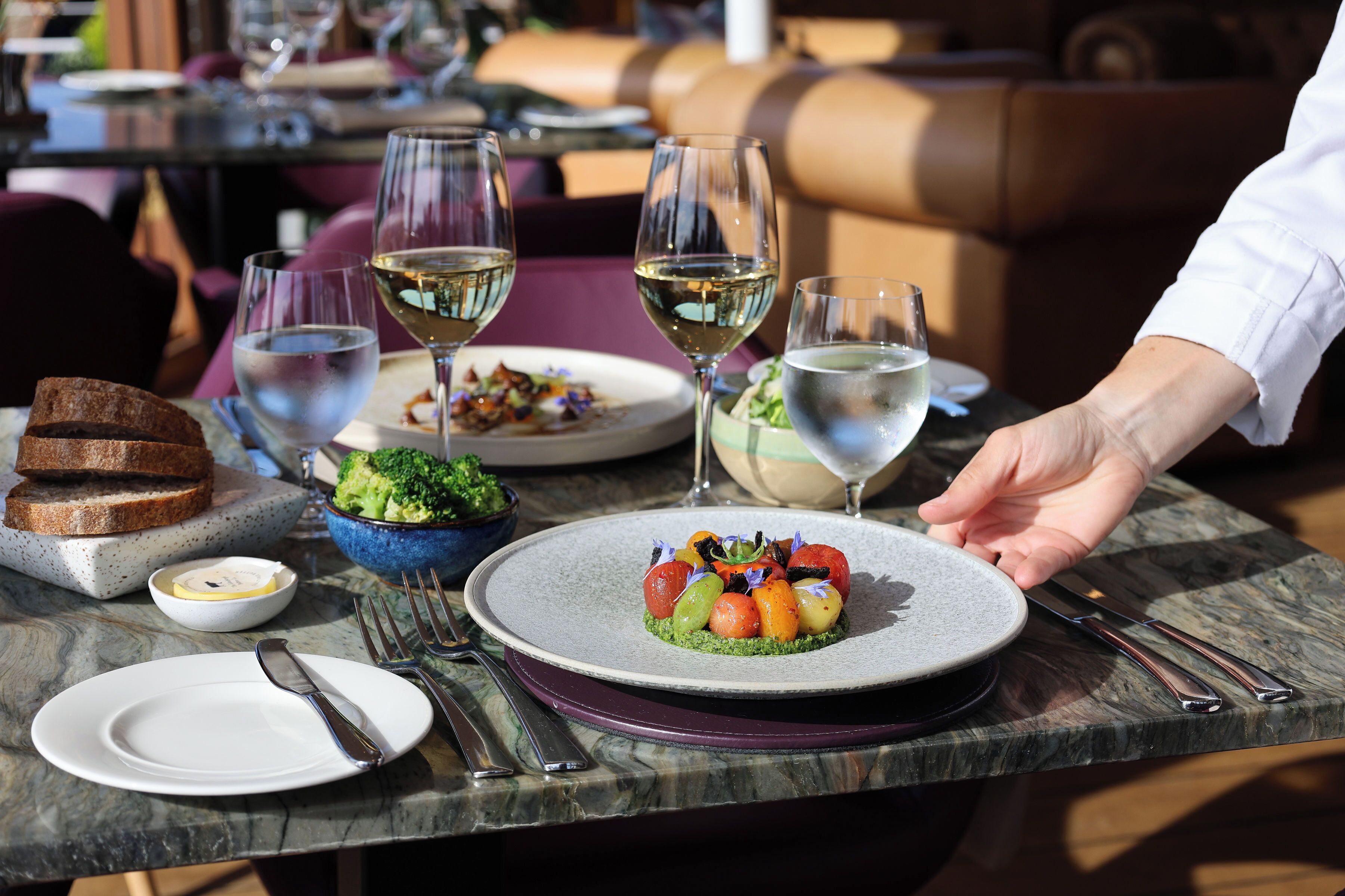 A dining table with plates, cutlery, and glasses of white wine.