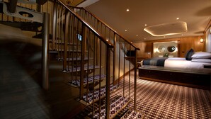 Una habitación de hotel moderna con una escalera en espiral, una cama grande y una alfombra estampada.