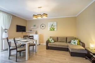 A modern living room with a dining area, a sofa set, a flat-screen TV, and a wall clock.
