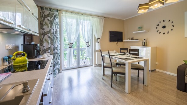 Eine moderne Küche mit Essbereich, großen Fenstern mit Vorhängen und einer Uhr an der Wand.