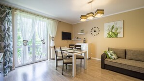 Ein modernes Wohnzimmer mit Essbereich, einer Couch, einem Fernseher und einem großen Fenster mit Vorhängen.