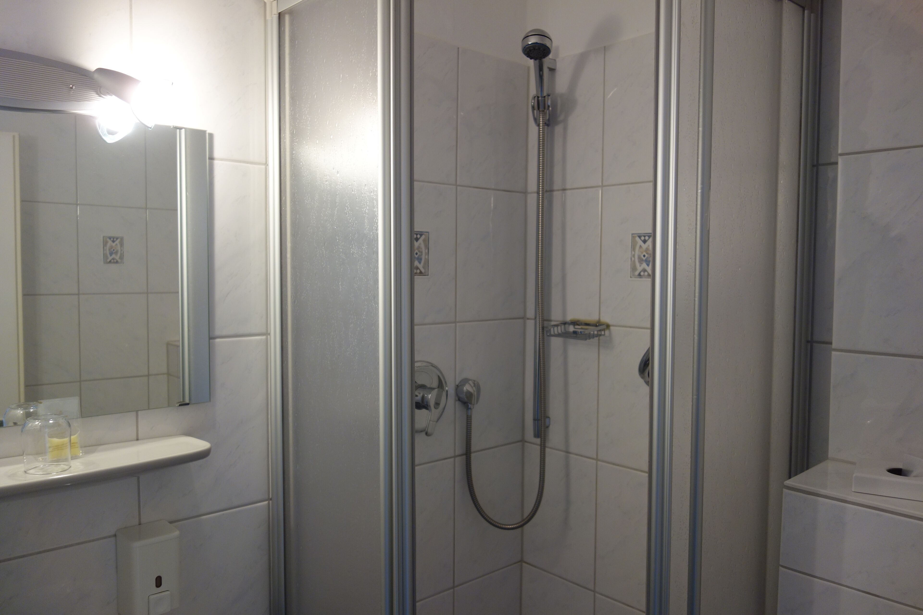Une salle de bain moderne avec une douche à parois de verre, un lavabo blanc avec un miroir et une petite étagère contenant des articles de toilette.