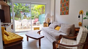 Ein Wohnzimmer mit einer Couch, einem gelben Sessel, einem Couchtisch aus Holz und einem Fernseher auf einem Holzständer.