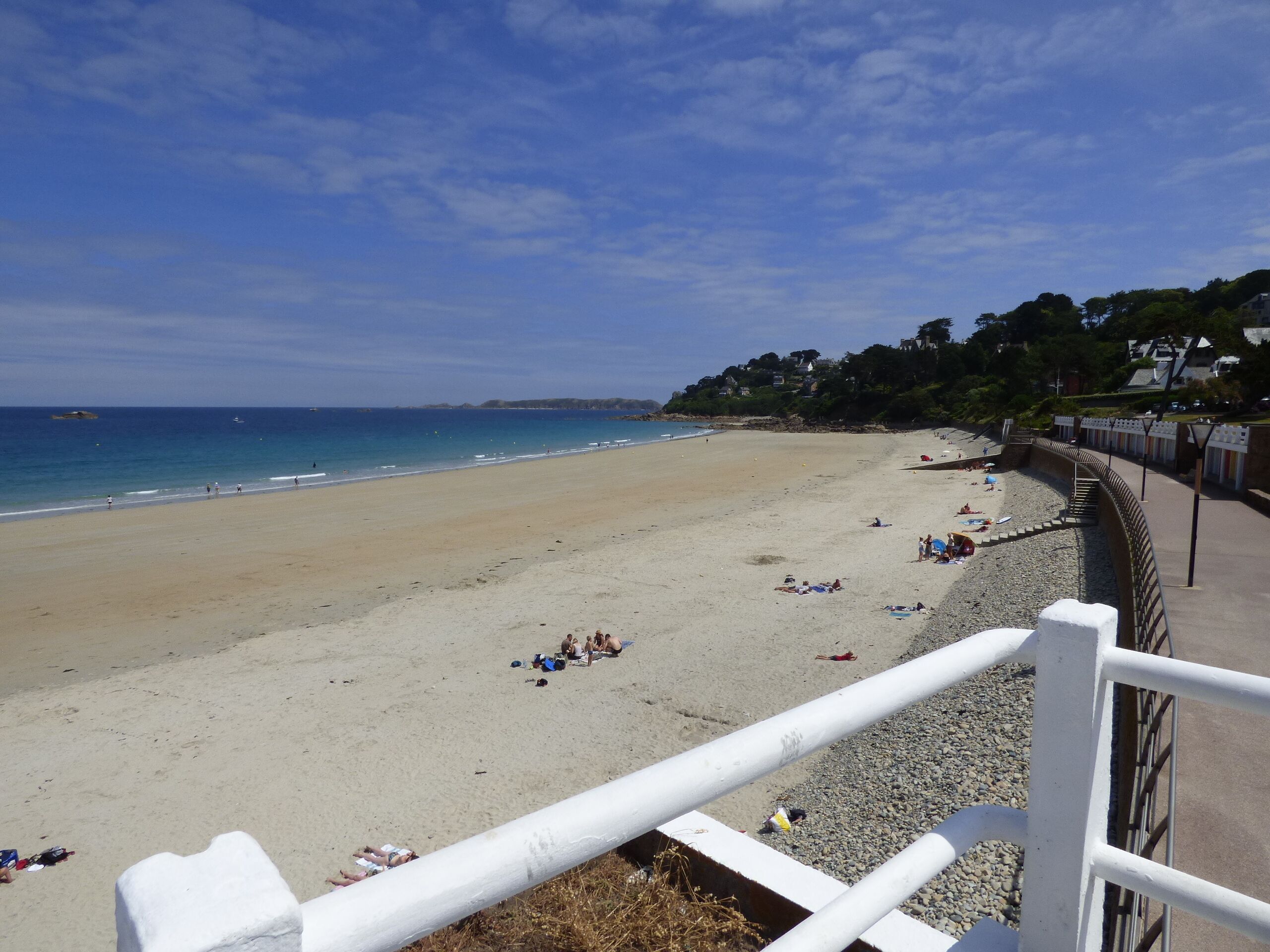 A beach with a white railing, clear blue sky, and calm sea.