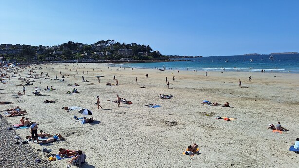 Ein Strand mit badenden und sonnenden Personen.