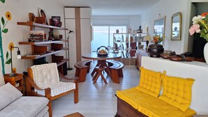 Ein Wohnzimmer mit einem gelben Sofa, Holzmöbeln und einem Essbereich mit einem runden Tisch.