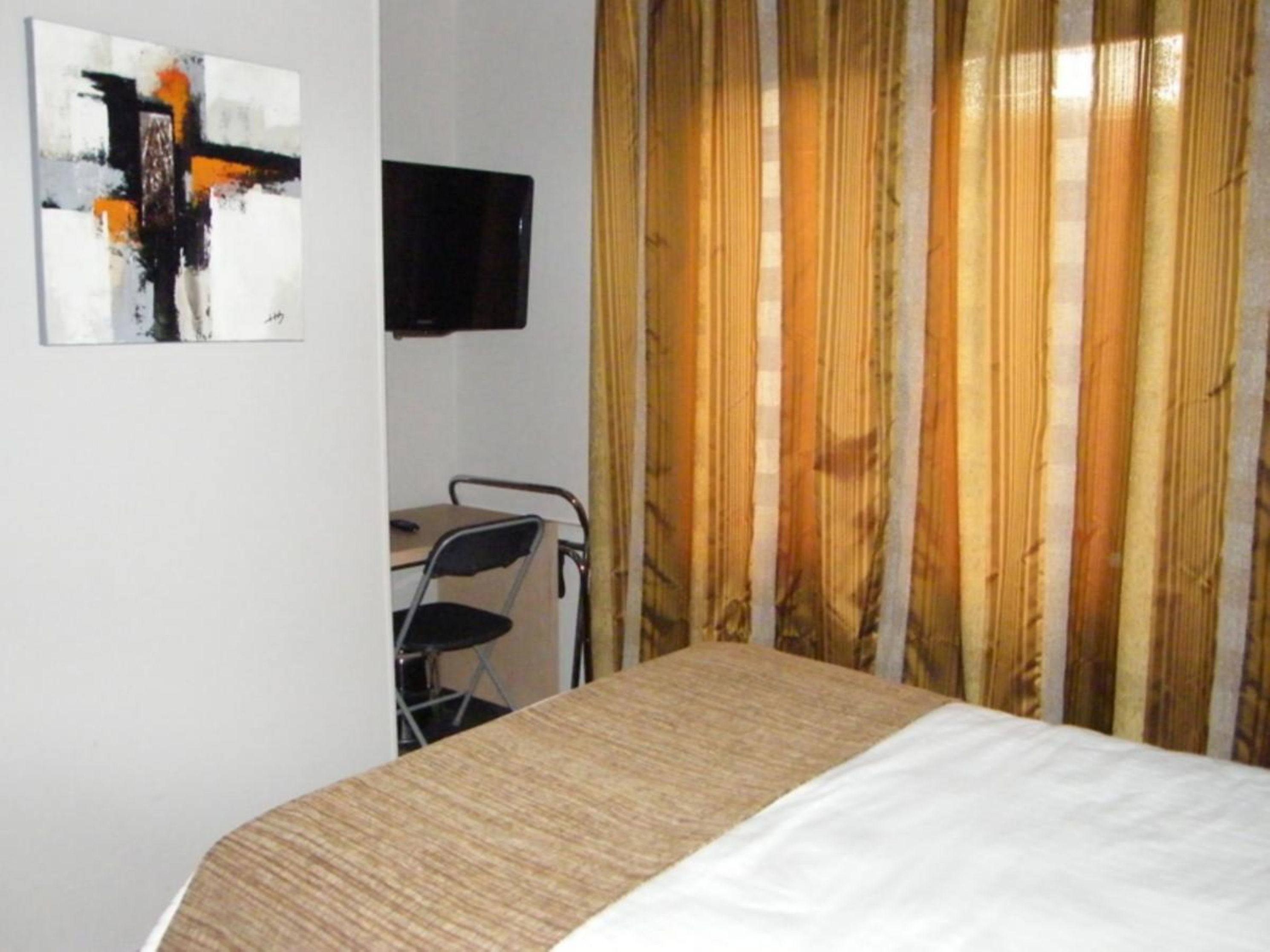 A hotel room with a bed, a desk, a chair, a television, and a painting on the wall.