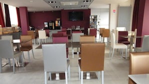 Un comedor moderno con varias mesas y sillas, un televisor de pantalla plana montado en la pared y una estantería al fondo.