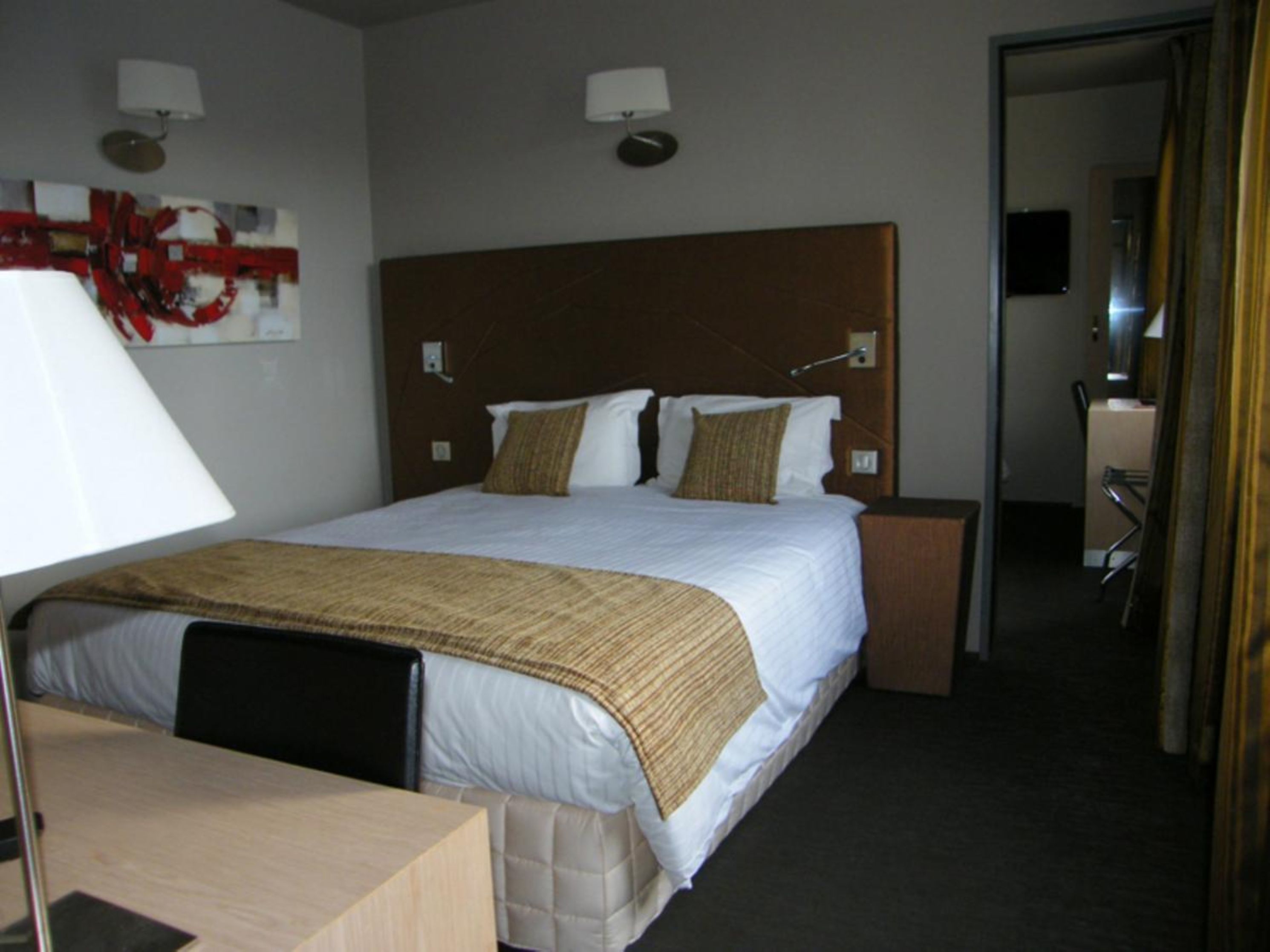 A hotel room with a large bed, a desk, a chair, and a mirror.