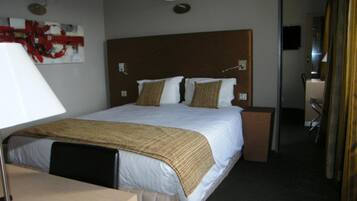 A hotel room with a large bed, a desk, a chair, and a mirror.