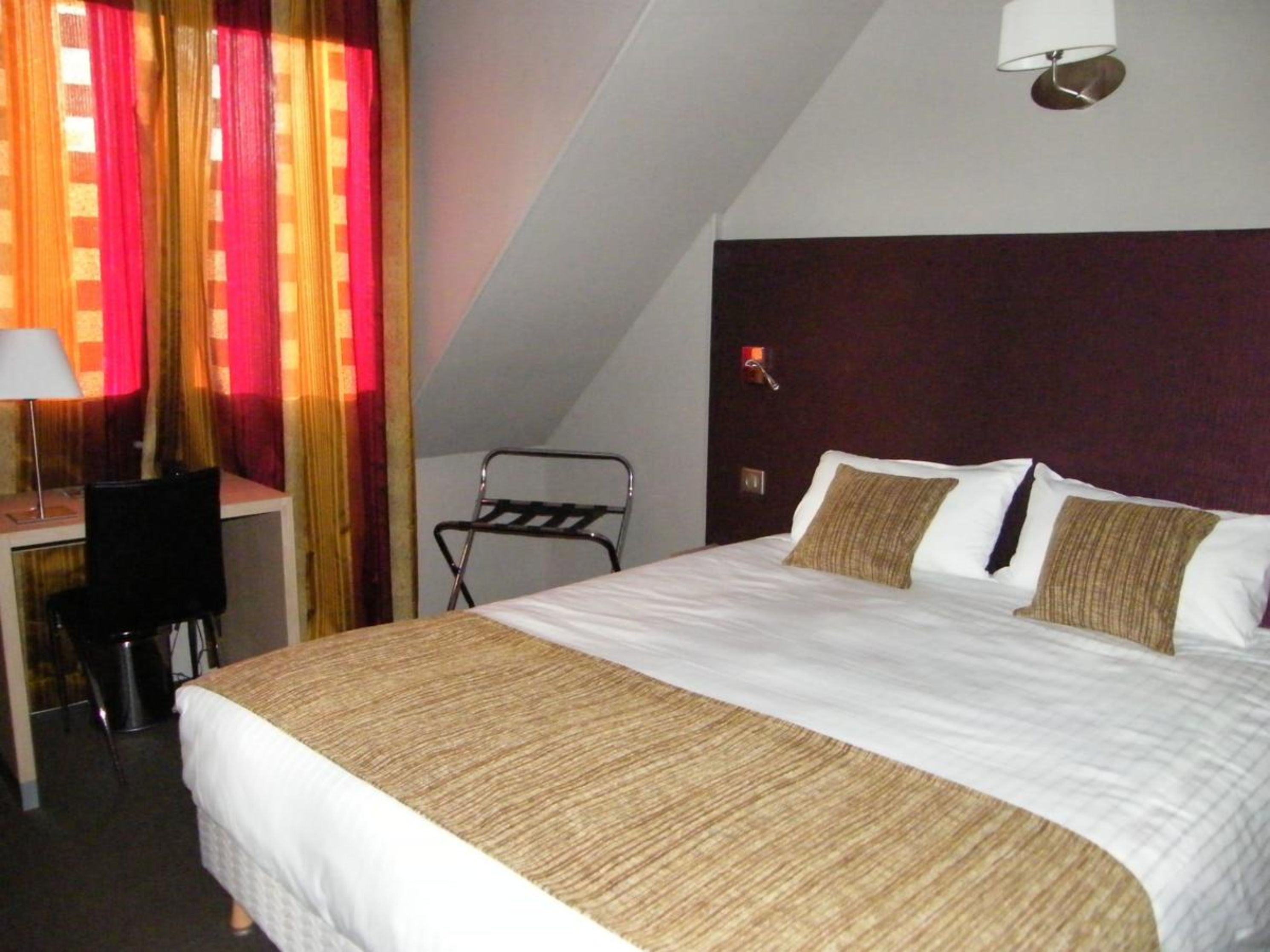 Een hotelkamer met een groot bed, een bureau met stoel, een lamp en een raam met gordijnen.
