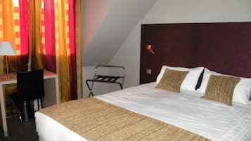 Een hotelkamer met een groot bed, een bureau met stoel, een lamp en een raam met gordijnen.