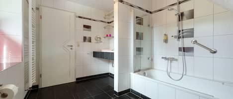 A modern bathroom with a glass-enclosed shower, a white bathtub, and a toilet.