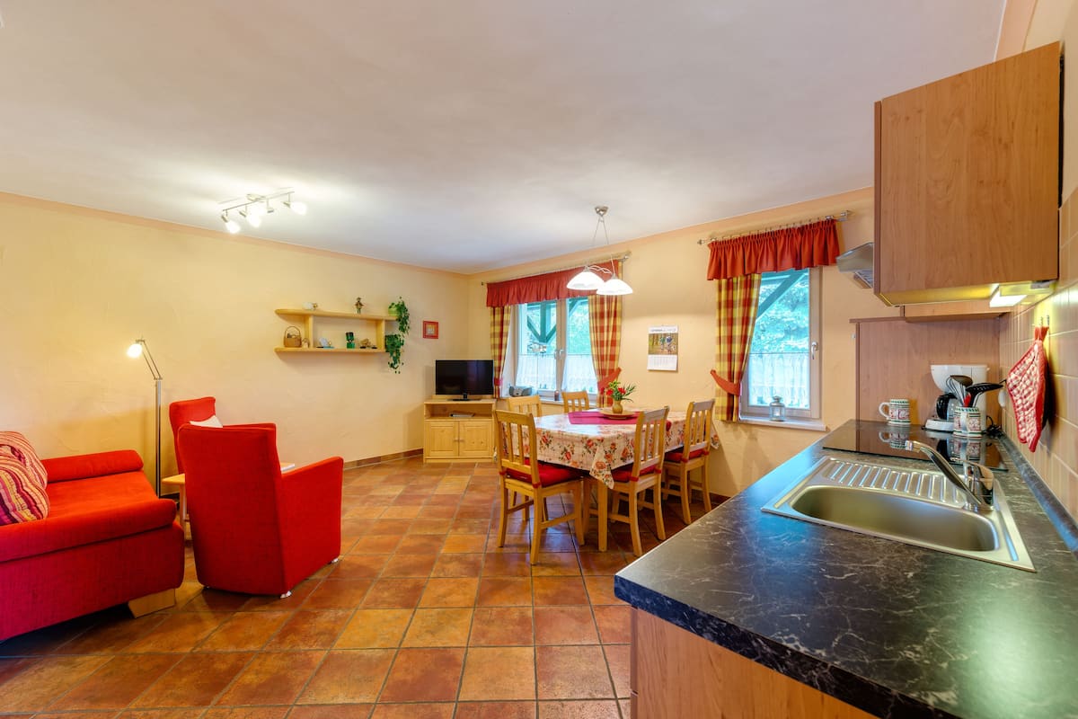 A compact kitchen with a dining area, a red sofa, and a TV.