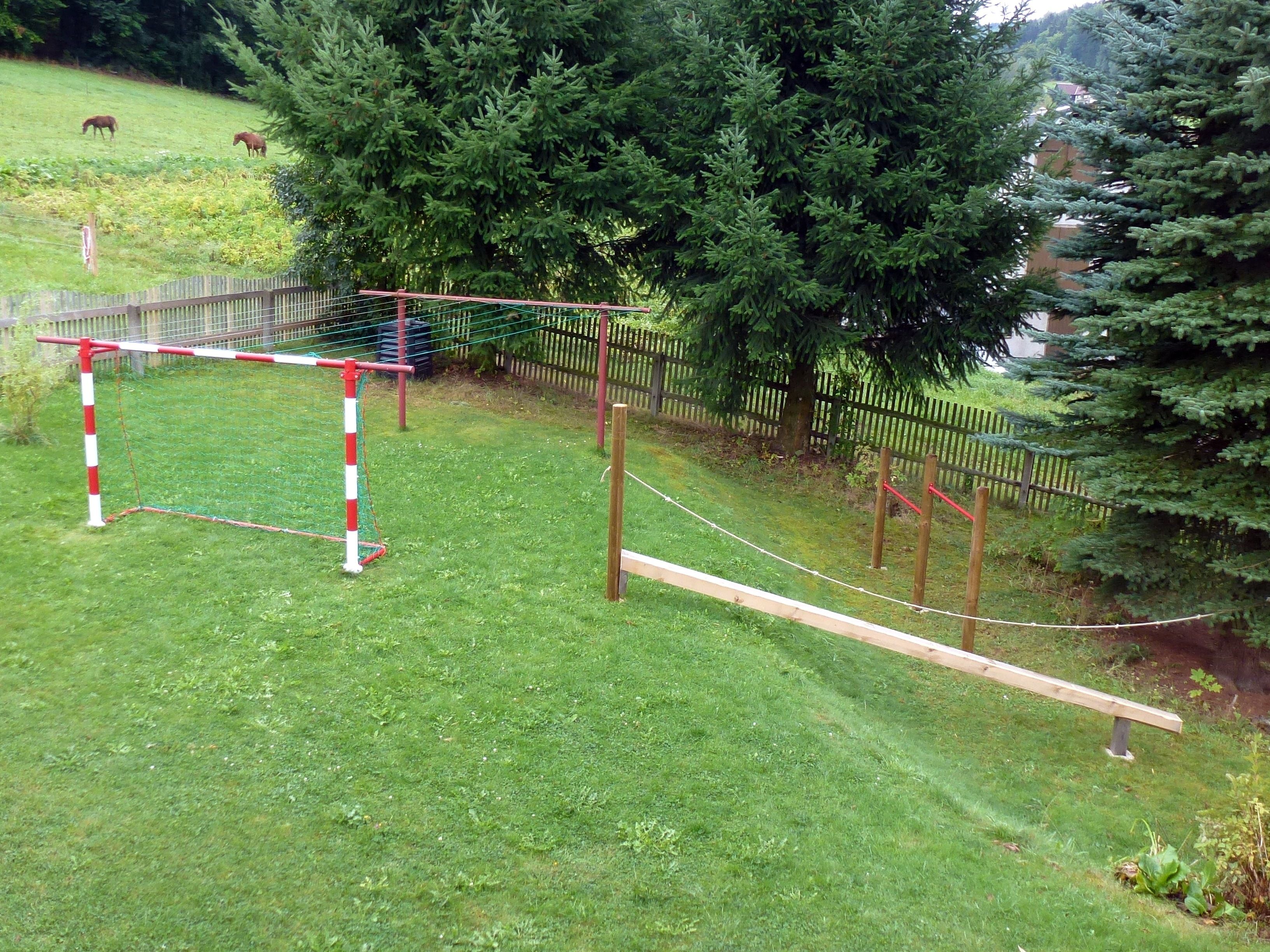 A fenced outdoor area with a wooden obstacle course, including a rope bridge and a small wooden platform.