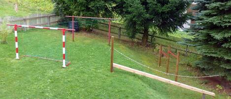 A fenced outdoor area with a wooden obstacle course, including a rope bridge and a small wooden platform.