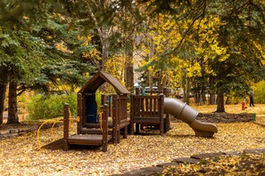 Un terrain de jeux avec un toboggan et des structures d’escalade, entouré d’arbres aux feuilles jaunes.