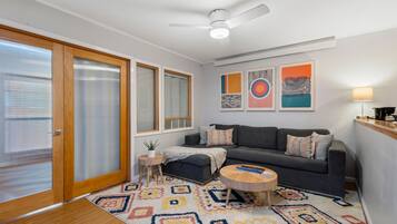 Una sala de estar moderna con un sofá gris, una mesa de centro redonda de madera y una alfombra colorida con estampado.