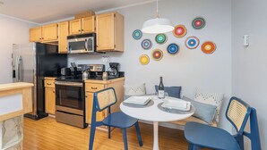 A compact kitchen with wooden cabinets, a stainless steel refrigerator, a microwave, and a stove. There is a dining area with a round table and blue chairs. - Centrally Located Condo | Walk to Gondola, Lift 8, Dining & River Trail (Telluride)