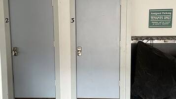 Dos puertas grises con los números 2 y 3, un letrero que indica estacionamiento exclusivo para inquilinos y un objeto negro en el suelo.