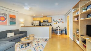 A modern apartment with a grey sofa, a small wooden table, a kitchen area, and a TV on a wooden shelf. - Centrally Located Condo | Walk to Gondola, Lift 8, Dining & River Trail (Telluride)