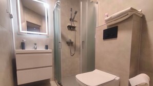 A modern bathroom with a glass-enclosed shower, a white toilet, a vanity with a mirror, and a black bath mat. - Studio Doris (Kraków)