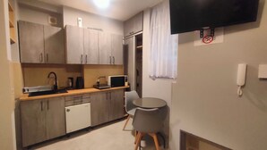 A compact kitchen with grey cabinets, a microwave, a sink, and a small dining table with a chair. - Studio Doris (Kraków)