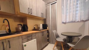 A compact kitchen with a sink, microwave, and a small refrigerator. There is a dining area with a table and two chairs. - Studio Doris (Kraków)