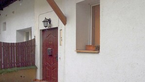 A red door with a mailbox, a small window with a shelf, and a wooden fence. - Studio Doris (Kraków)