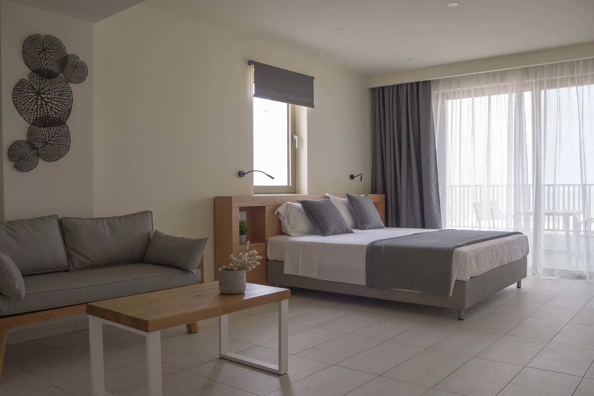 A modern bedroom with a bed, a sofa, a bedside table, and a window with curtains.