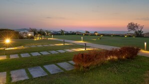 Ein angelegter Garten mit Steinwegen, einer grünen Rasenfläche und Blick auf das Meer im Abendlicht.
