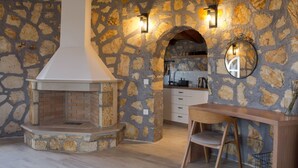 Eine Küche mit Steinwänden, einem eingebauten Kamin, Holzbalkendecke und einem Essbereich mit Holztisch und Stuhl.