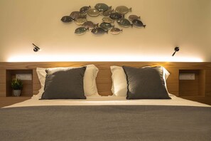Un dormitorio con una cama grande, dos mesitas de noche, una decoración de peces colgada en la pared y una pequeña planta en maceta.