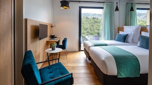 A modern hotel room with a large bed, a desk with a chair, a small table with a plant, and a view of the mountains through the window. - Hotel Sainte Victoire (Vauvenargues)