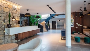 A modern lobby with a stone wall, a wooden reception desk, a spiral staircase, and a seating area with a sofa and chairs. - Hotel Sainte Victoire (Vauvenargues)
