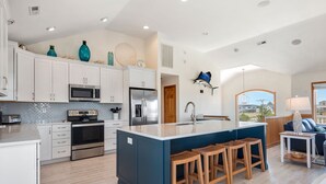 A spacious kitchen with white cabinets, stainless steel appliances, and a central island with stools. - Wise Choice: Semi-oceanfront | Private Pool | Spa (Nags Head)