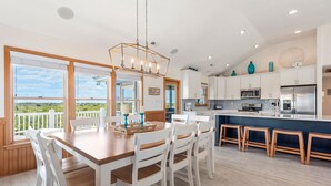 A modern kitchen with white cabinets, a wooden dining table, and a view of the outdoors. - Wise Choice: Semi-oceanfront | Private Pool | Spa (Nags Head)