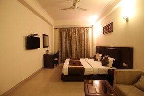 A hotel room with a bed, a desk, a chair, a television, and a ceiling fan. - Hotel The Tanish (New Delhi)