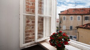 Una ventana con una maceta roja en el alféizar, un marco blanco y una pared de ladrillo.