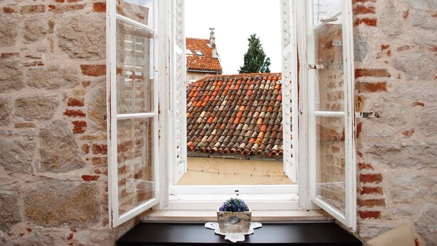 Una ventana abierta con vistas a un edificio de ladrillo y un tejado de tejas.