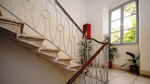 Una escalera con barandilla metálica, plantas en macetas y una ventana con vista a follaje.