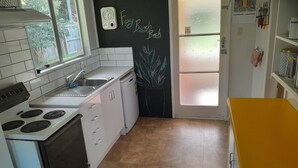 Una cocina con armarios blancos, una estufa, un lavamanos y una pizarra con la inscripción 'Foxy Beach Bach'.