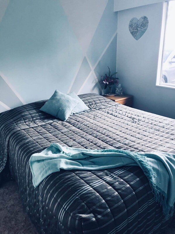 A bedroom with a bed, a nightstand, a potted plant, and a heart-shaped decoration on the wall.