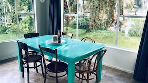 Un comedor con mesa turquesa y sillas de madera oscura, ventanas amplias con vistas a un jardín.